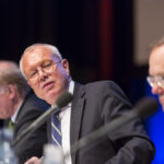 Podiumsdiskussion sind lebhafter. Auf dem Podium werden fachliche Scharmützel ausgetragen. Georg Crezelius auf der Bühne mit Michael Korth (li.), Thomas Eisgruber (Bayerisches Staatsministerium der Finanzen) und Michael Wendt (BFH, rechts).